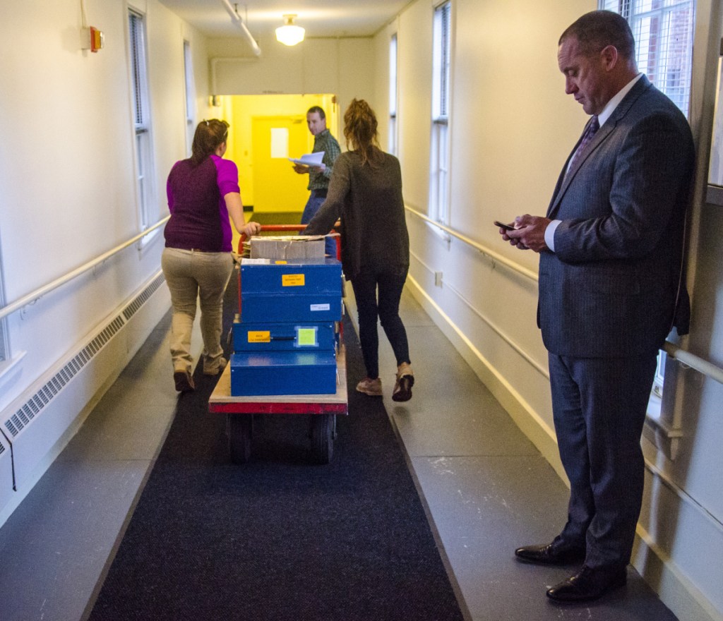 Josh Tardy, attorney for the Bruce Poliquin campaign, right, observes the chain of custody as Department of the Secretary of State staffers move ballots Thursday afternoon in the Elkins Building in Augusta.