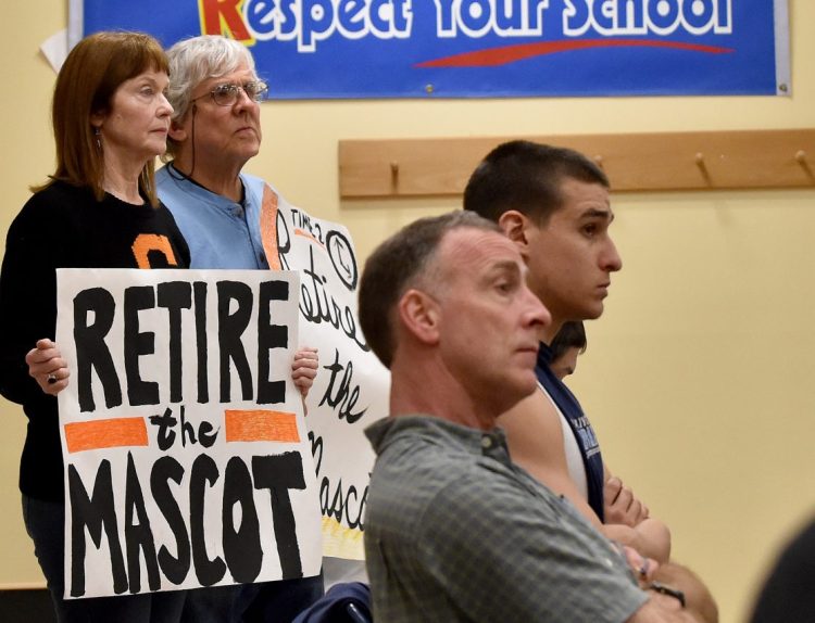 Linda Savage, back left, and Mark Roman, back center, stand with signs calling for the retirement of the Skowhegan Area High School Indian mascot during a Skowhegan school board meeting at Skowhegan Middle School on April 7, 2016.