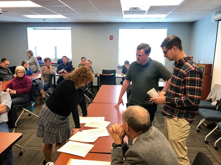 Waterville City Clerk Patti Dubois, left, presents disputed ballots to Todd Martin, of the Sustain Mid-Maine Coalition, right center; Waterville Mayor Nick Isgro, far right; and City Attorney Bill Lee, seated, after the recount of votes on the referendum on plastic shopping bags.