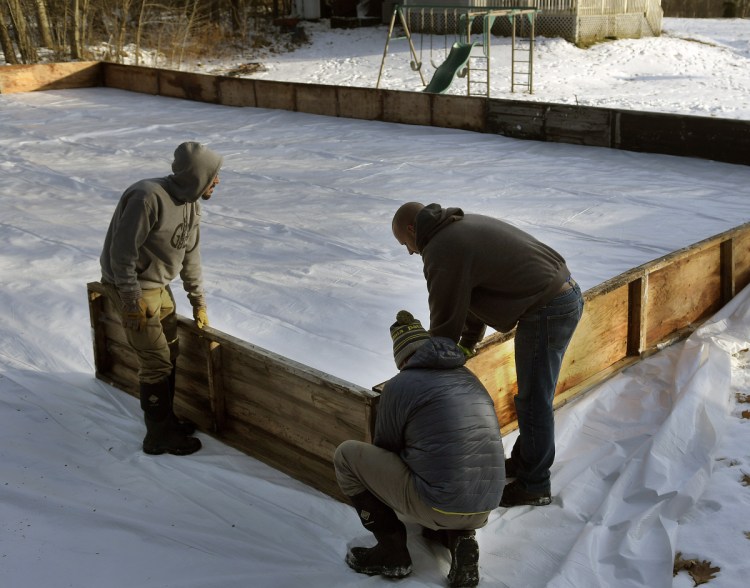 Trevor Knell, left, Ryan Cote, and Tom Langlois stake the boards of an ice rink Sunday in the back yard of Langlois' Monmouth home. The men's children play hockey together.