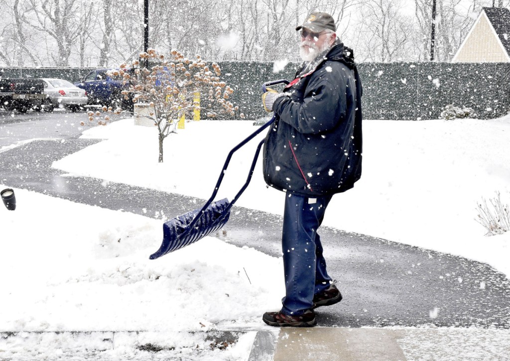 City of Waterville employee Bob LaPlante kicks sticky snow off his shovel while clearing sidewalks Tuesday at the Waterville police station.