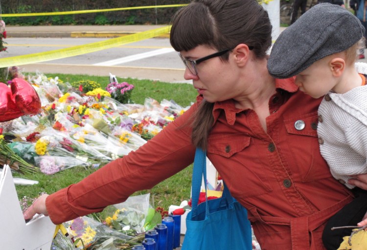 Kathleen Fuller, holding her son Garrick, places a stone on a star of David at a memorial in front of Tree of Life synagogue in Pittsburgh on Wednesday. The massacre underscores the dilemma of law enforcement in assessing the risk of people making online rants when social media is so ubiquitous.