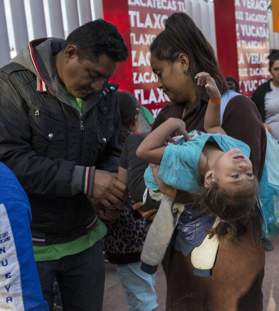 A Central American family, left, waits in line to begin the asylum process in Tijuana, Mexico on Friday. Above, a woman prays at a temporary shelter after her caravan group arrived in Tijuana on Friday.