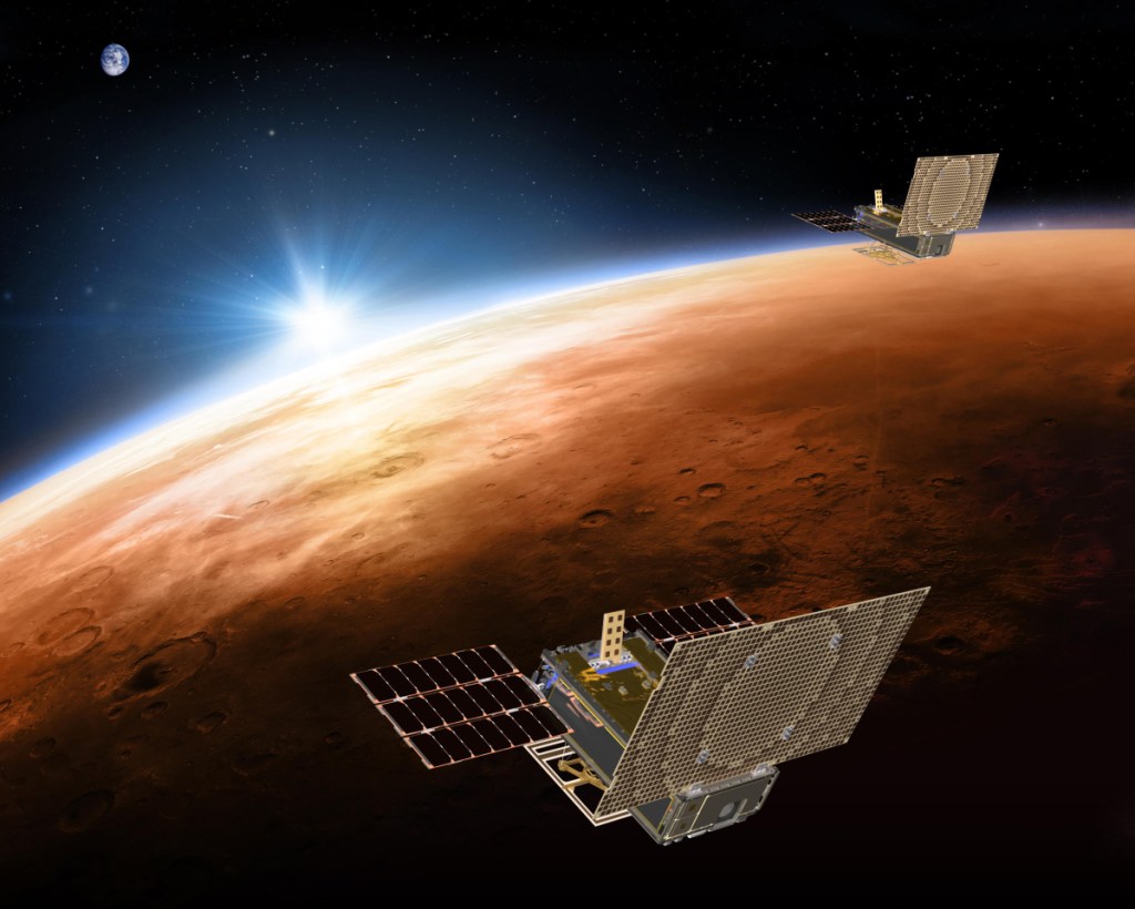 This illustration made available by NASA in March 2018 shows the twin Mars Cube One project, or MarCO, spacecrafts flying over Mars with Earth and the sun in the distance. The MarCOs will be the first CubeSats, a kind of modular, mini-satellite, flown into deep space.