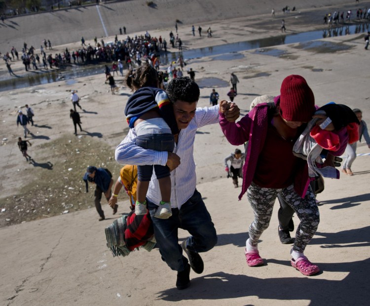 Migrants ascend a riverbank heading to the U.S. border after pushing past police in Tijuana, Mexico. Some who reached the fence were met with tear gas.