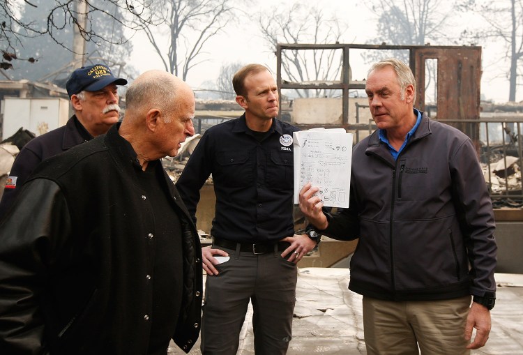 California Gov. Jerry Brown looks at a student's work book, held by Interior Secretary Ryan Zinke, that was found in the fire-ravaged Paradise Elementary School on Wednesday. The school is among the thousands of homes and businesses destroyed when a wildfire burned through Paradise last week.