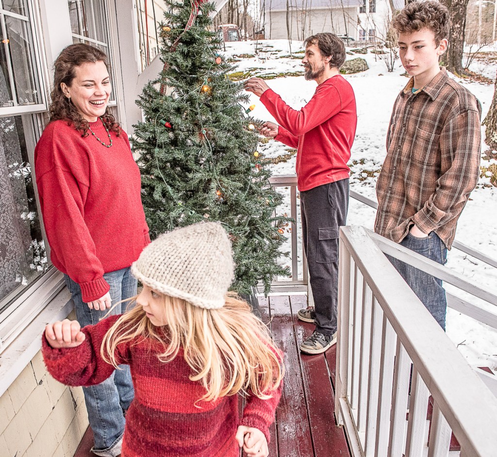 D'Arcy Ames and her partner, Gary Couture, hang lights on their outdoor Christmas tree at their Auburn home with the help of children Vivian and Calvin. The family is facing severe financial hardship and risks losing the house as Couture recovers from Lyme disease.