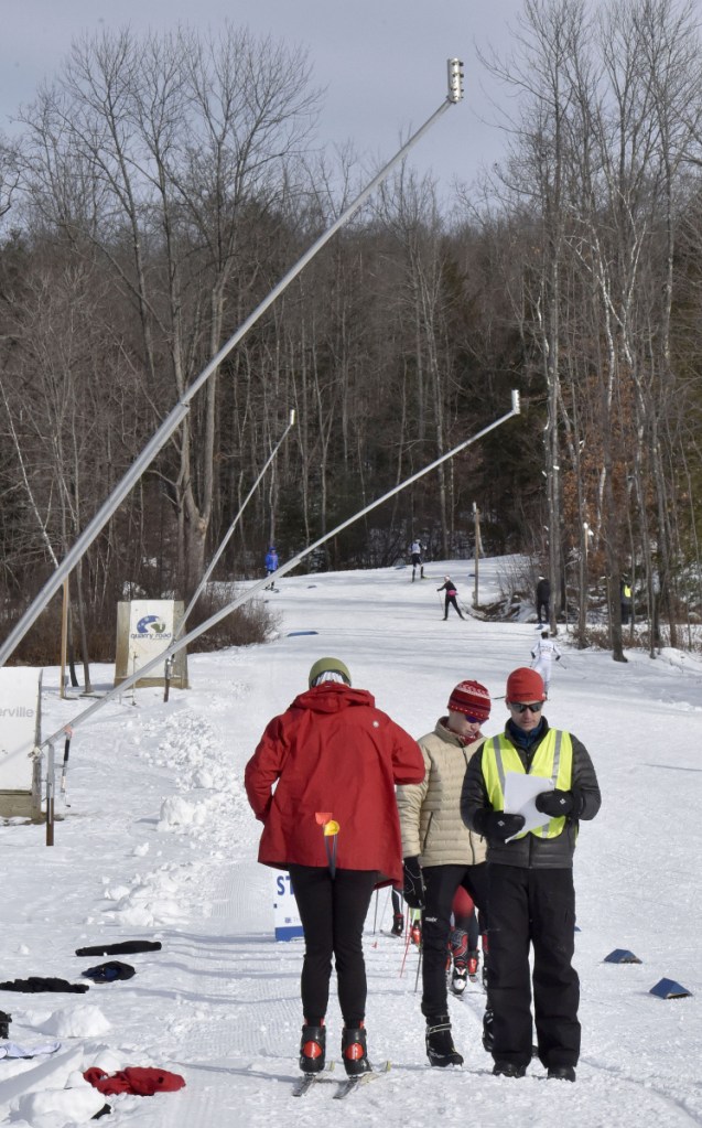 Under snowmaking guns along trails volunteer Kirk Ross, right, checks cross-country skiers assembled at the start for races during the Quarry Road Opener in Waterville on Sunday.