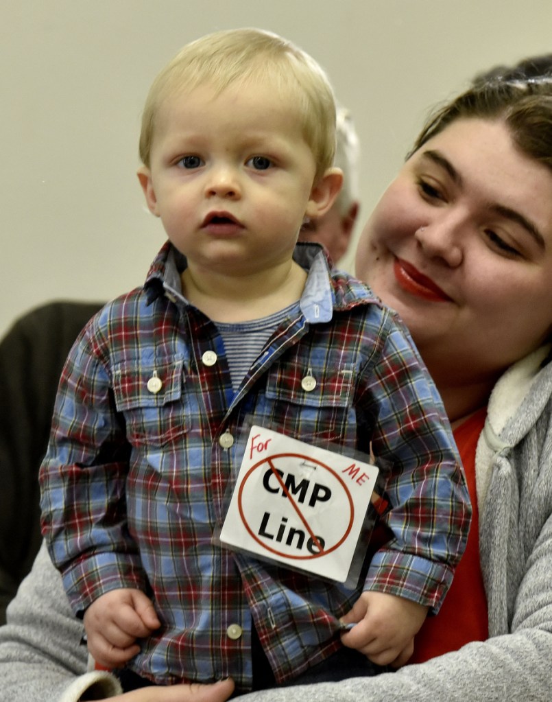 Mysadie Ayotte holds her son Xander, who wore a sign protesting CMP's New England Clean Energy Connect project prior to a meeting with Somerset County Commissioners in Skowhegan on Wednesday.