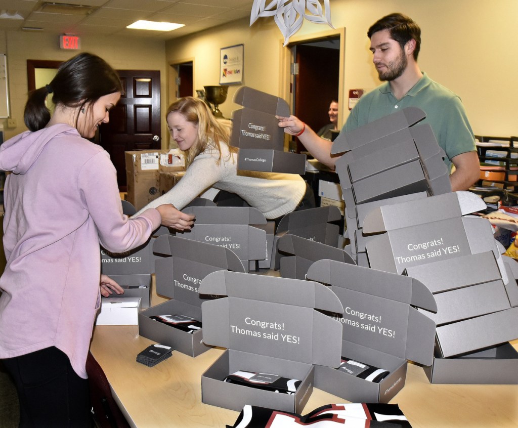 Thomas College staff members — from left, Cassidy Pinkham, Abby Dooley and Alan Wood — create gift packages Wednesday that will be sent to new students recently accepted to the Waterville college.