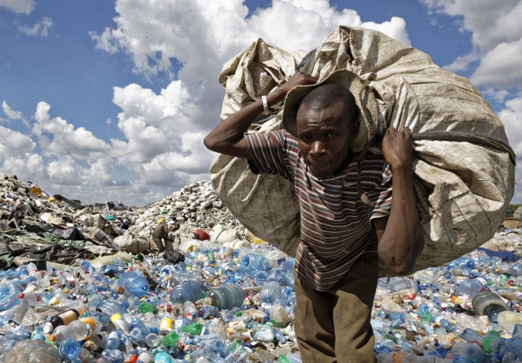 A man walks on a mountain of plastic bottles as he carries a sack of them to be sold for recycling after weighing them at the dump in the Dandora slum of Nairobi, Kenya.