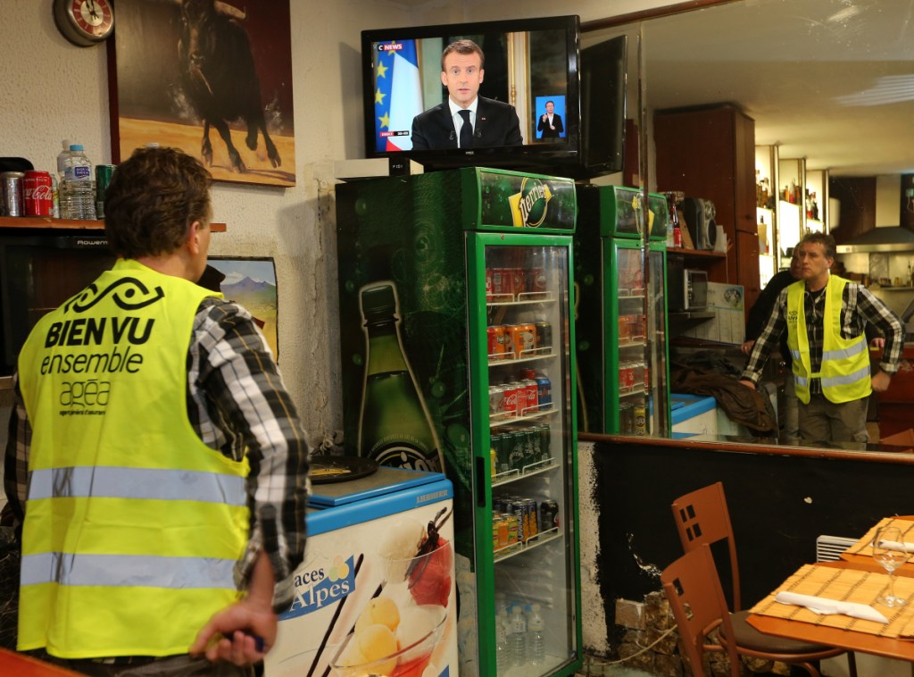 Yohann Piedagnel watches French President Emmanuel Macron during a televised address to the nation, in Hendaye, southwestern France, Monday. In an unusual admission, French President Emmanuel Macron says he's partially responsible for anger fueling protests.