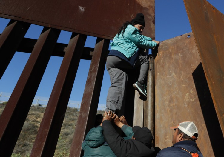 Honduran migrants help a woman scale a section of the border wall to San Diego on Wednesday so she could turn herself in and apply for asylum. President Trump's border wall proposal has led to a stalemate in budget negotiations.