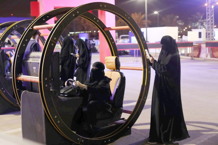 A Saudi woman takes a photo as another woman tries out a car driving simulator in Riyadh, Saudi Arabia. The nation lifted the world's only ban on women driving in June.