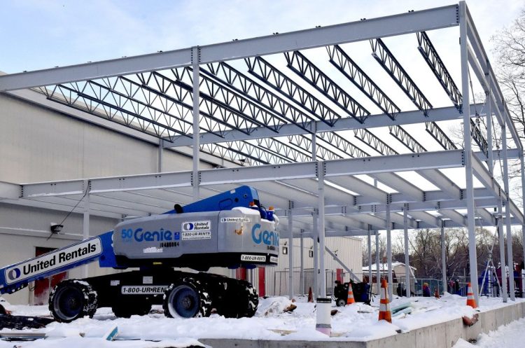 As children play on an outdoor playground, background, workers erect steel girders Thursday for the new Family Wellness Center at the Alfond Youth Center on North Street in Waterville. The building permit for the structure was discounted, which private developer Paul Lussier criticized at Wednesday's City Council meeting.