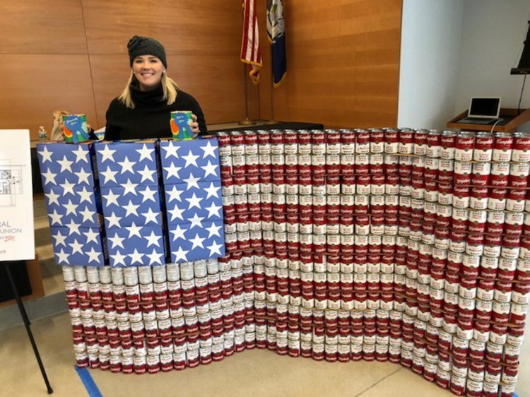 Alexandra Fabian, marketing and business development specialist for KV Federal Credit Union, stands on Saturday behind an American Flag sculpture made of Campbell's soup cans and Honey Maid graham cracker boxes. The entry won Best in Show and Community Choice awards during a statewide Day of Service event in the Chace Community Forum in downtown Waterville.