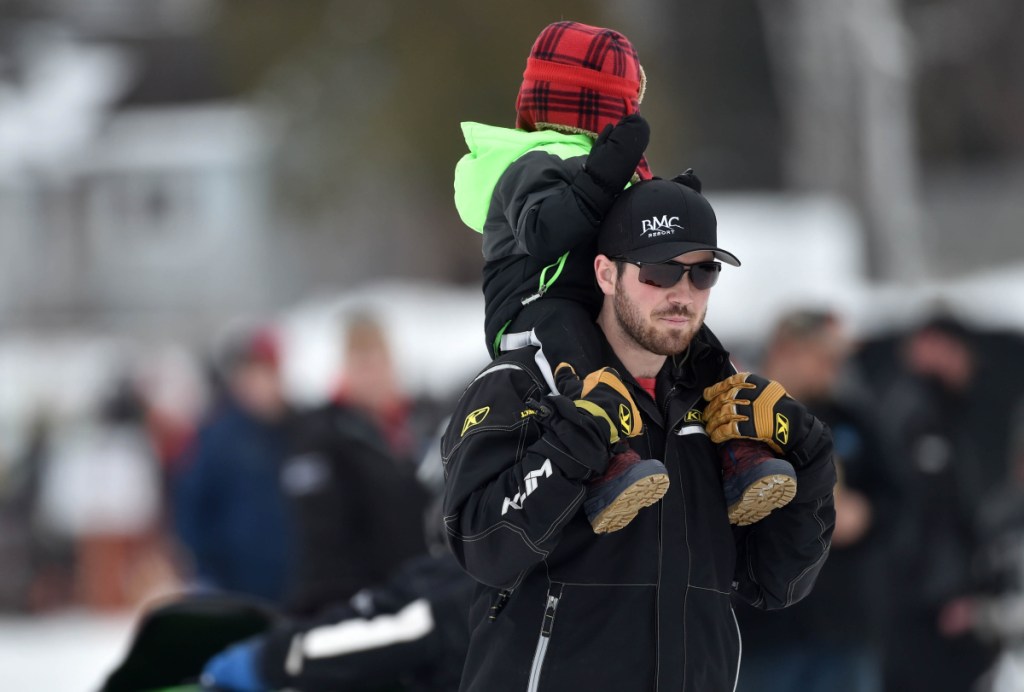 Courtney Ellis walks around the snowmobiles on display with his sone Saul atop his shoulders at the Snodeo in Rangeley on Friday, Jan. 21, 2017. 