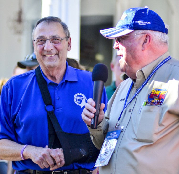 Gov. Paul LePage, left, smiles as Peter Prescott, who was the first to drive through the Great Race Arch, speaks to the crowd on Water Street on June 26 in Gardiner.