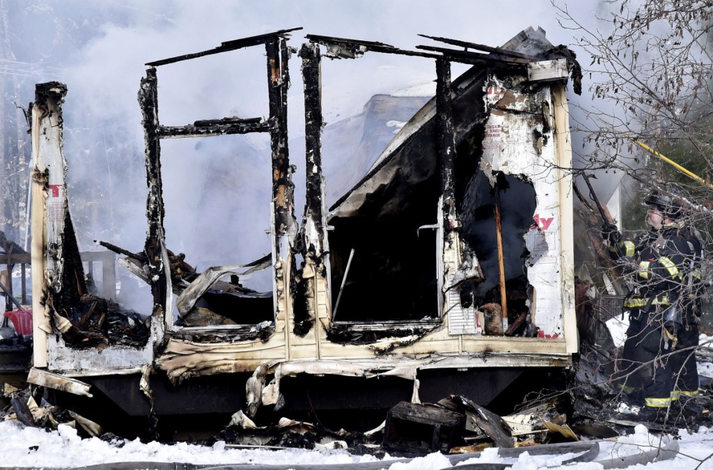 Firefighters pull burnt siding off a smoking mobile home on U.S. Route 2 in Norridgewock that was destroyed by fire on Wednesday.