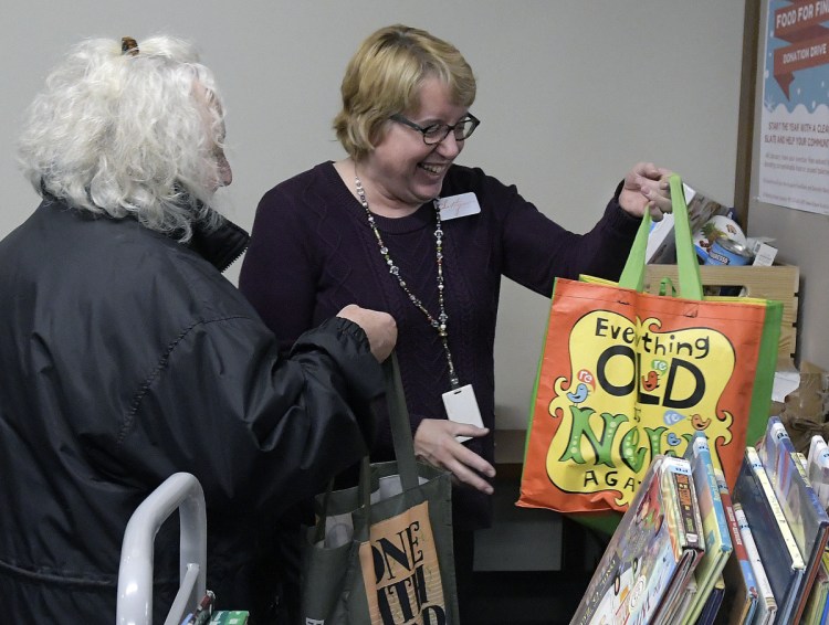 Pat Greve, left, hands Lithgow Public Library employee Kathy Petersen bags of toiletries and food at the front desk Wednesday in Augusta. The library is running a fine forgiveness program through the end of January permitting cardholders to donate nonperishable food and essential items in exchange for having their overdue fines forgiven. Greve, of Hallowell, donates her time at the library.