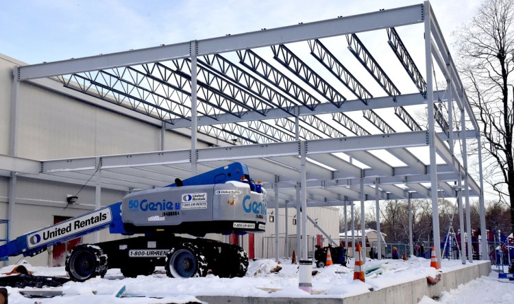 As children play on an outdoor playground, background, workers erect steel girders Jan. 3 for a new Wellness Center at the Alfond Youth Center in Waterville. The center has paid the city of Waterville the full permit fee for the expansion.