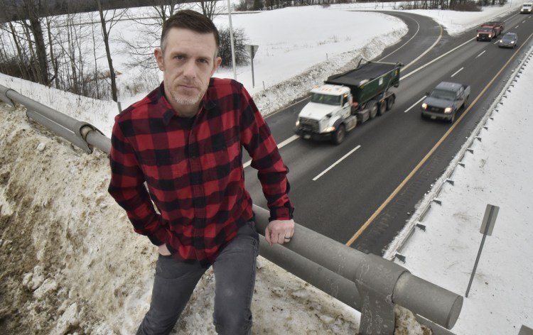 Ben Wheeler sits on a railing banked with snow Wednesday on the Trafton Road overpass on Interstate 95 in Waterville. Wheeler said a Waterville plow truck pushed heavy snow over the railing, and that the snow dropped 15 feet onto his car as he was driving north, causing an estimated $7,000 worth of damage to the front windshield and the roof.