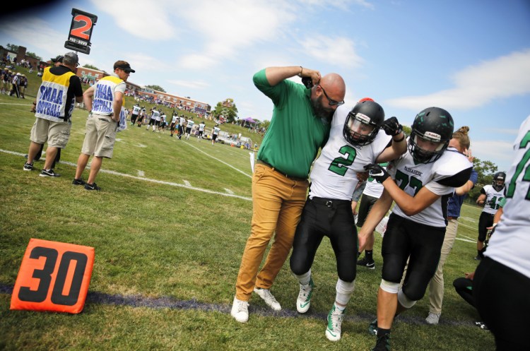 Massabesic's assistant coach Ethan Magill and teammate Robert Woods help junior Owen Roberts off the field last season after he was hurt in a game against Cheverus in Portland. Maine does not require medical coverage in "collision" sports.