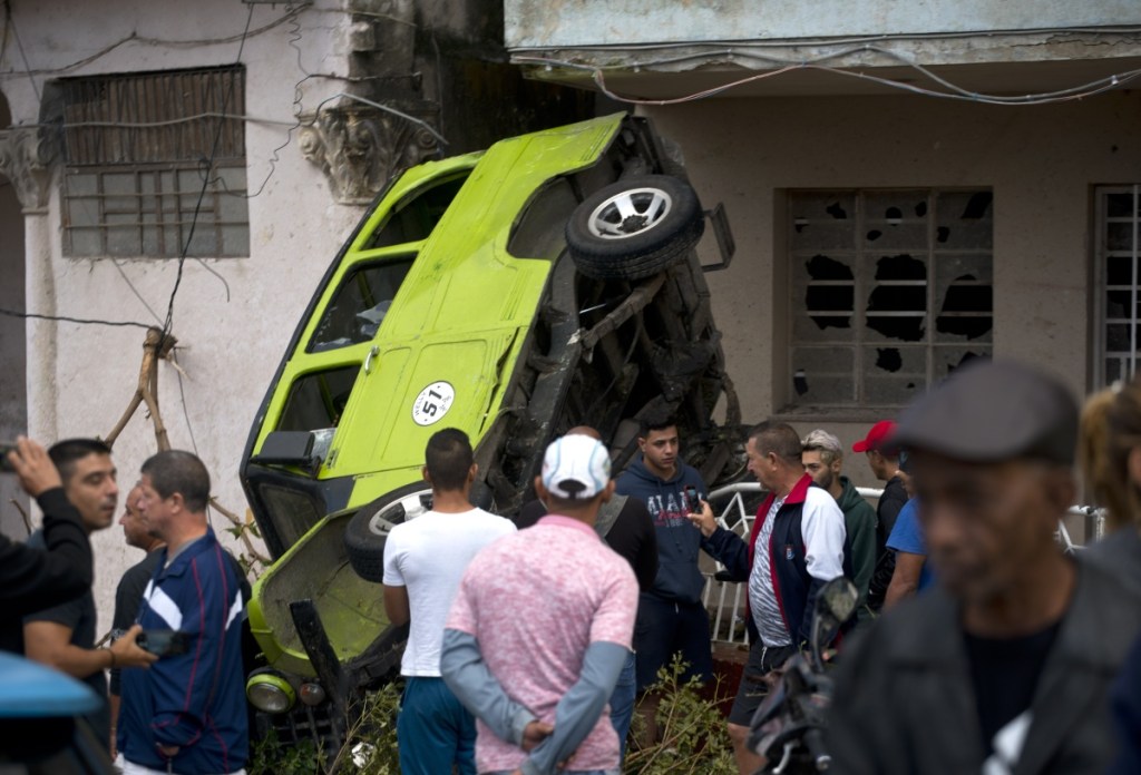 People stand around a car that was overturned by a tornado in Havana, Cuba, Monday. A tornado and pounding rains smashed into the eastern part of Cuba's capital overnight, toppling trees, bending power poles and flinging shards of metal roofing through the air as the storm cut a path of destruction.