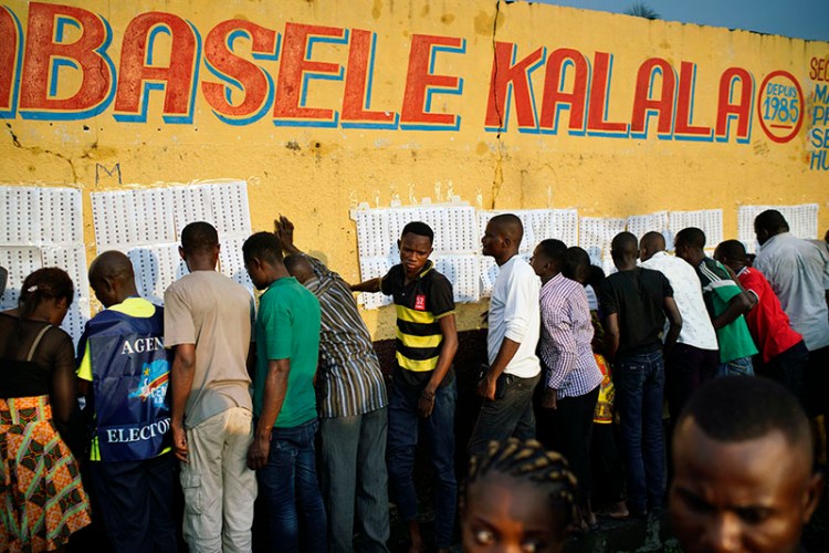 Election officials tape voter registration lists to a wall of the Les Anges primary school in Kinshasa, Congo, as voters start to check their names on Dec. 30.
