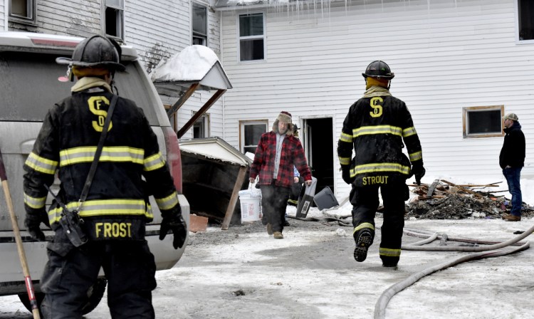 At center, a man carries items past Skowhegan firefighters from the home at 386 Water St. in Skowhegan after fire broke out there Sunday.