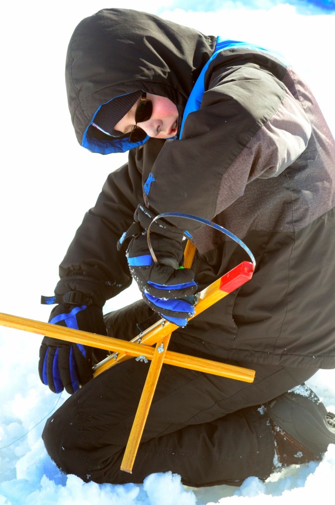 After his trap's flag was tripped but there was no fish on the hook, Mcgyver Blundon resets the trap before putting it back into a hole in the ice Saturday during a children's ice fishing derby on Cochnewagon Lake in Monmouth.