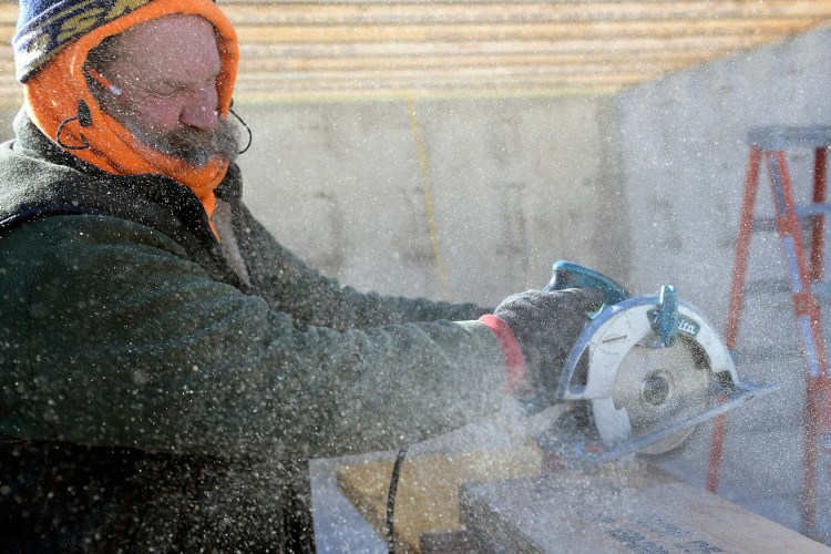 Brad Ellis cuts beams on Tuesday in 25 mph wind at a home that his firm, BHS Inc., is building in Farmingdale. Ellis said the work continues with his crew despite the frigid conditions since he has several months of work booked. "You get it done," he said.