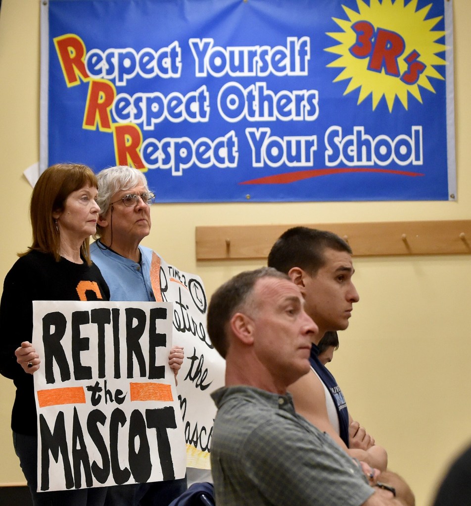 Lisa Savage, back left, and Mark Roman, back center, stand with signs calling for the Skowhegan Area High School Indian mascot be retired during an April 7, 2016, School Administrative District 54 board meeting at Skowhegan Area Middle School. 