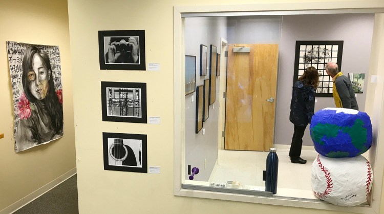 Showgoers look at a self-portrait by Maranacook Community High School student Ruslan Reiter on April 28, 2017, during Raw Space Augusta Art Walk in downtown Augusta. The exhibition was a pop-up event that showcased visual and performing arts in downtown Augusta's vacant storefronts and offices.