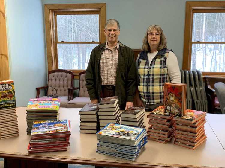 Carol Eckert’s husband, Jeff Frankel, left, and Julie Bailey, project organizer, with the 120 volumes recently donated to Carol’s Corner by Scholastic.