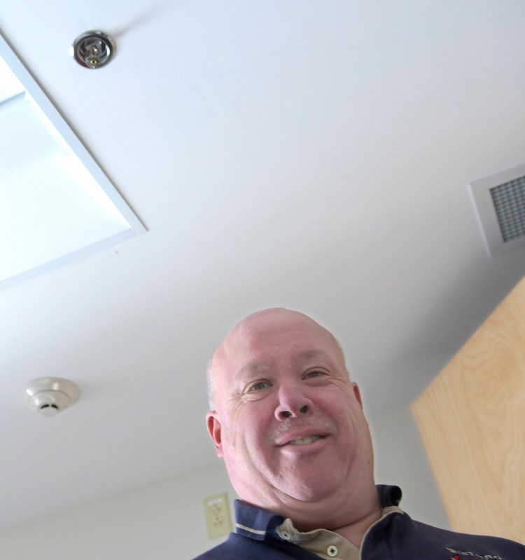 Winthrop Fire Chief Dan Brooks beneath a sprinkler and smoke detector at the town's fire station Thursday in Winthrop. Brooks is recommending the town adopt an ordinance requiring sprinklers in new, residential subdivisions — a housing area of three or more homes or a multi-dwelling complex.