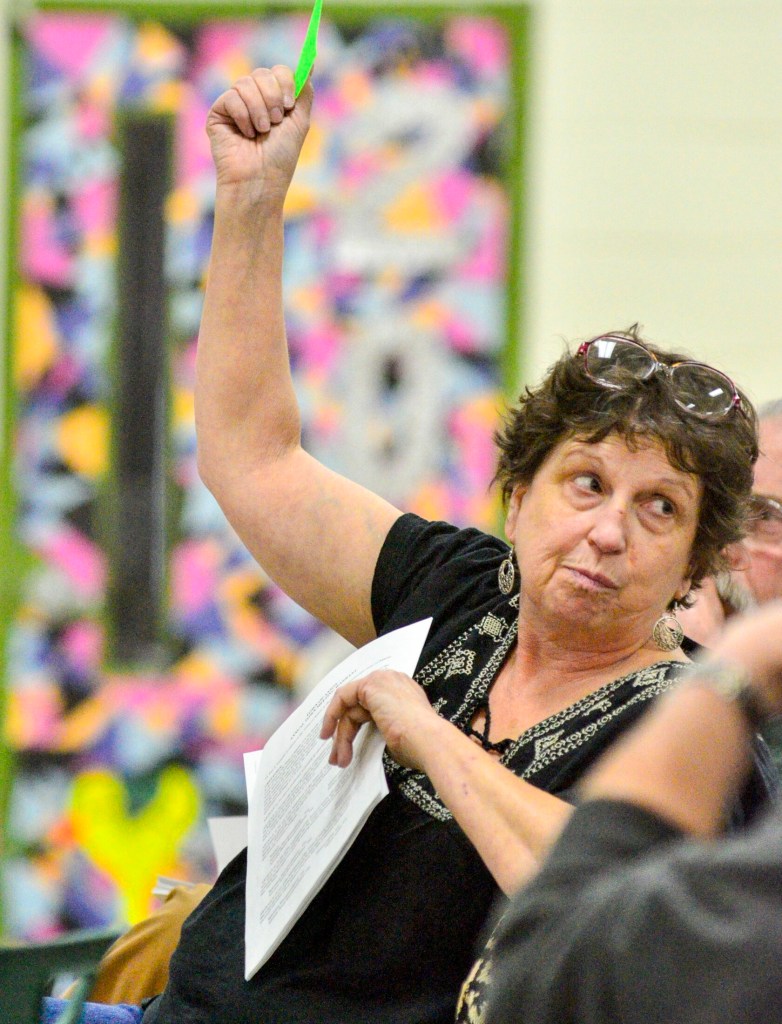 Janice Miller holds up a card to vote Saturday during the Anson Town Meeting, held in the Carrabec High School gymnasium.