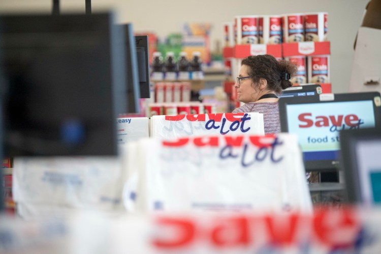 Margaret Withee, a cashier at Save-a-Lot, stands at her register with plastic bags that cost 10 cents each draped over the register partitions at Save-A-Lot in downtown Waterville on March 15.