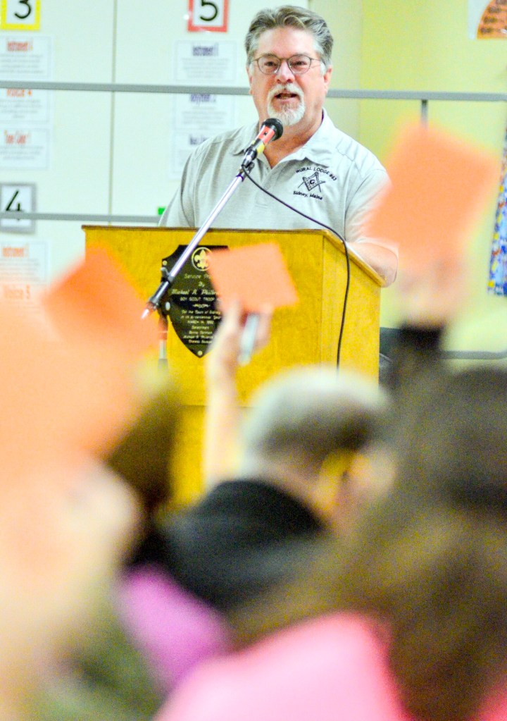 Moderator Doug Eugley looks over residents voting by holding up cards Saturday during Town Meeting at James H. Bean School in Sidney.