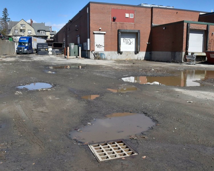 A delivery truck passes through a nearly dry parking lot behind stores in The Concourse in Waterville on Monday. The lot was flooded with several feet of muddy water from a broken water main on Sunday. Firefighters used a boat and an officer in the water to locate the drain, foreground, before unplugging it to free the water.  