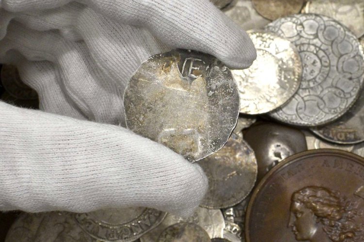In this Sept. 9, 2021 photo provided by auctioneer Morton & Eden Ltd., a rare 17th century one shilling coin is displayed above a metal box containing other coins, at the auction house, in London. (Menelaos Danellis/Morton & Eden Ltd. via AP)