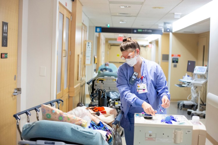 Registered nurse Cassandra Pateneaude cares for a patient in a busy hallway in the emergency department at Maine Medical Center earlier this month.