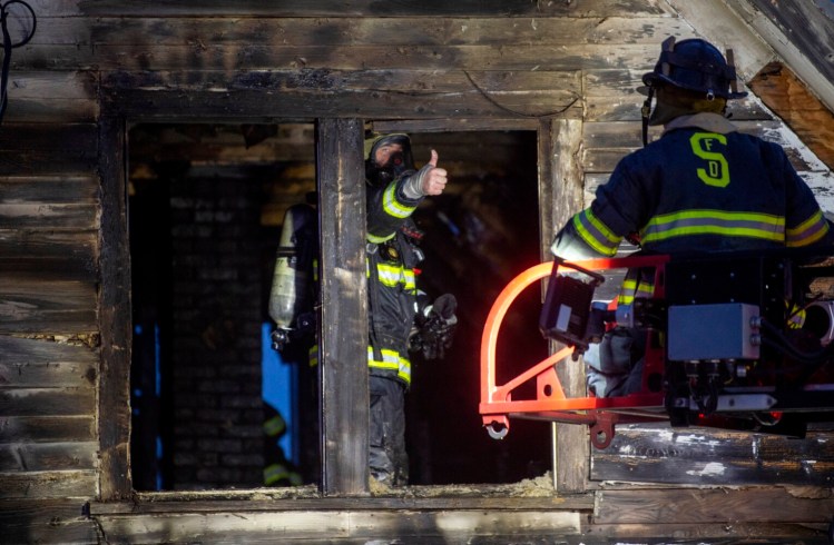 A firefighter gestures to another from the second floor of a Skowhegan home that burned Friday near the Skowhegan fairgrounds.