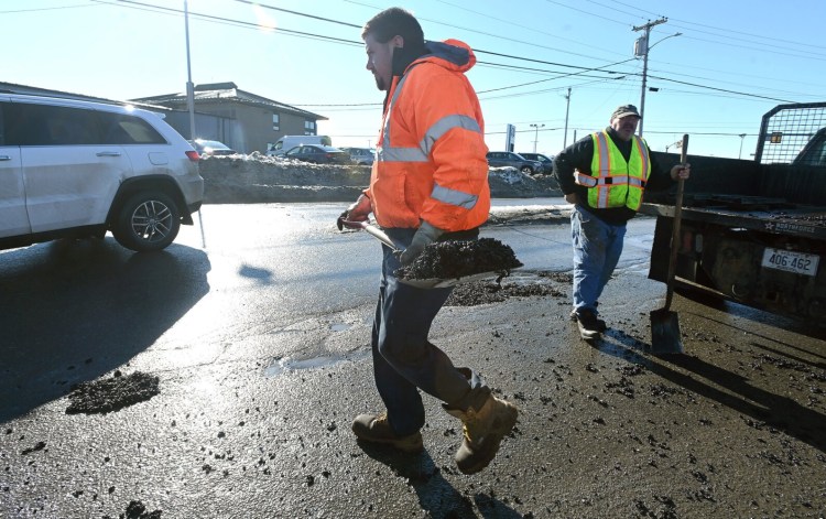 Waterville Public Works employee Bobby Bellows carries a scoop of cold asphalt patch Wednesday as he works to fill potholes on Armory Road in Waterville.