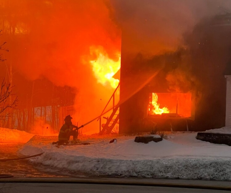 A firefighter kneels in the snow Saturday night as he douses a blaze at a century-old duplex home on Tallwood Drive in Readfield.