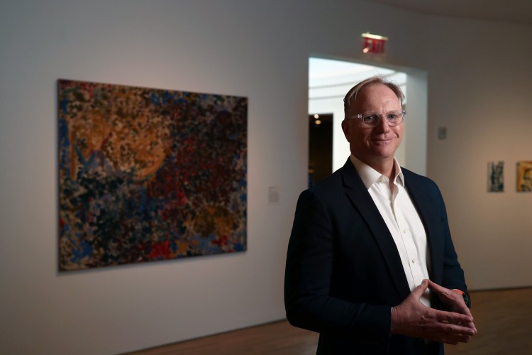 ROCKLAND, ME - MARCH 18: Farnsworth Museum director Christopher Brownawell stands next to "Saha," left, one of four of the museum's Lynne Mapp Drexler paintings. The museum is selling two Drexler paintings, just as she's gaining more notoriety, to help fund new works for their collection to better diversify. Drexler lived on Monhegan Island until she died in 1999. The Farnsworth sold one of her paintings at auction this month for $1.2 million. (Staff photo by Ben McCanna/Staff Photographer)