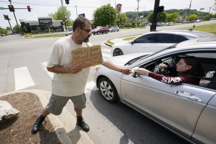 Adam Atnip, who lives in his car, accepts money from a driver as he panhandles on May 10 in Cookeville, Tenn. 