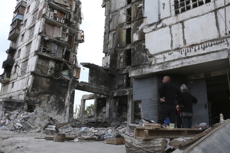 Local residents stand at the side of a damaged building during a heavy 