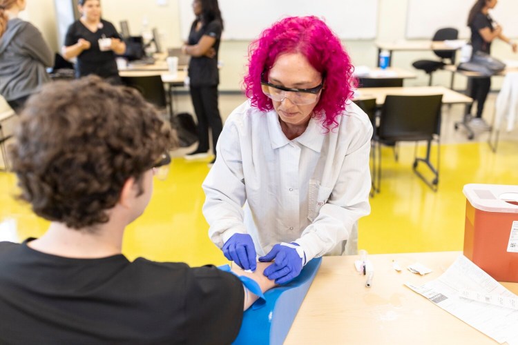 Melissa Joudrey practices a blood draw on a fellow student at a phlebotomy training class. The class, which is held at SMCC is a work training program through NorDx. 