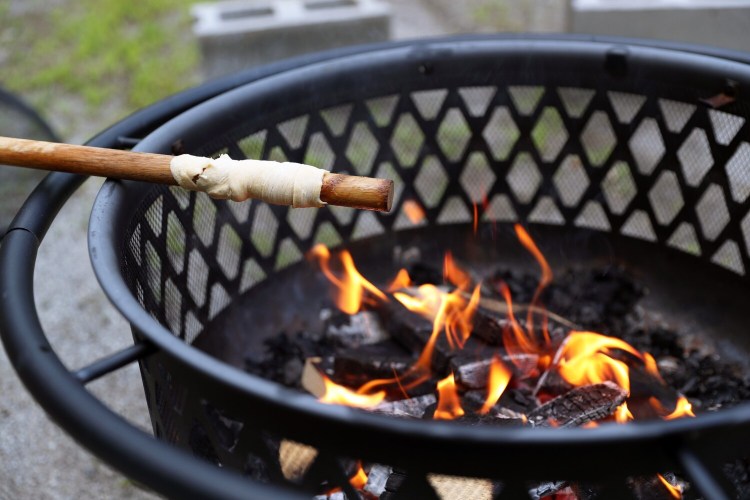 A dough-wrapped wooden dowel cooks over a campfire to make a dough boy, a time-honored campfire treat. 